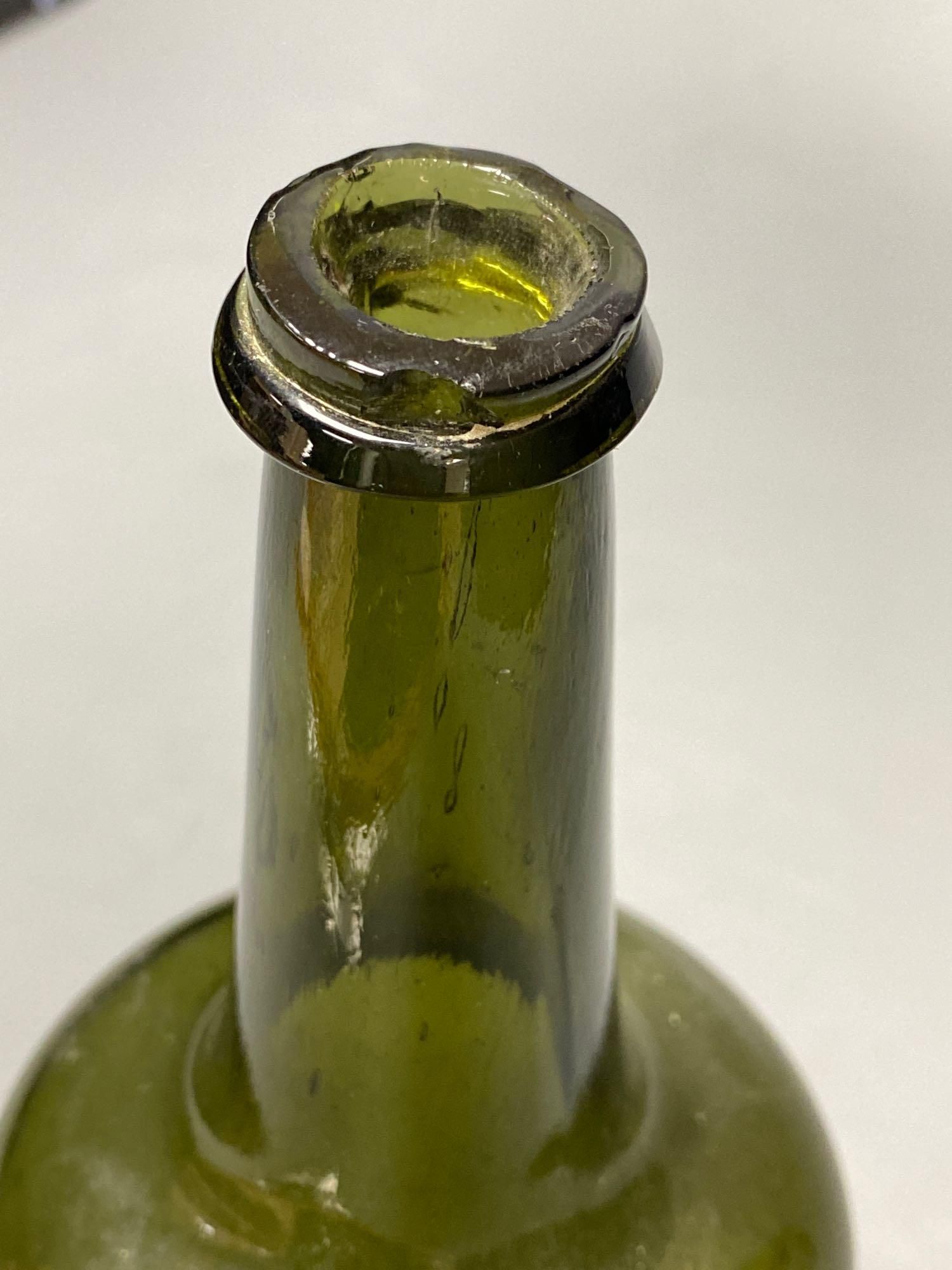 An early 18th century dark green glass wine bottle with a kick in based, 23cm